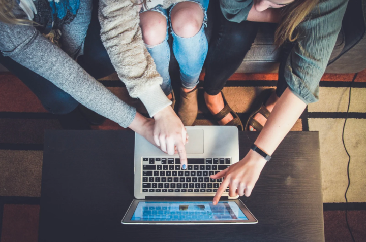 a teenager and two adults point at a laptop screen